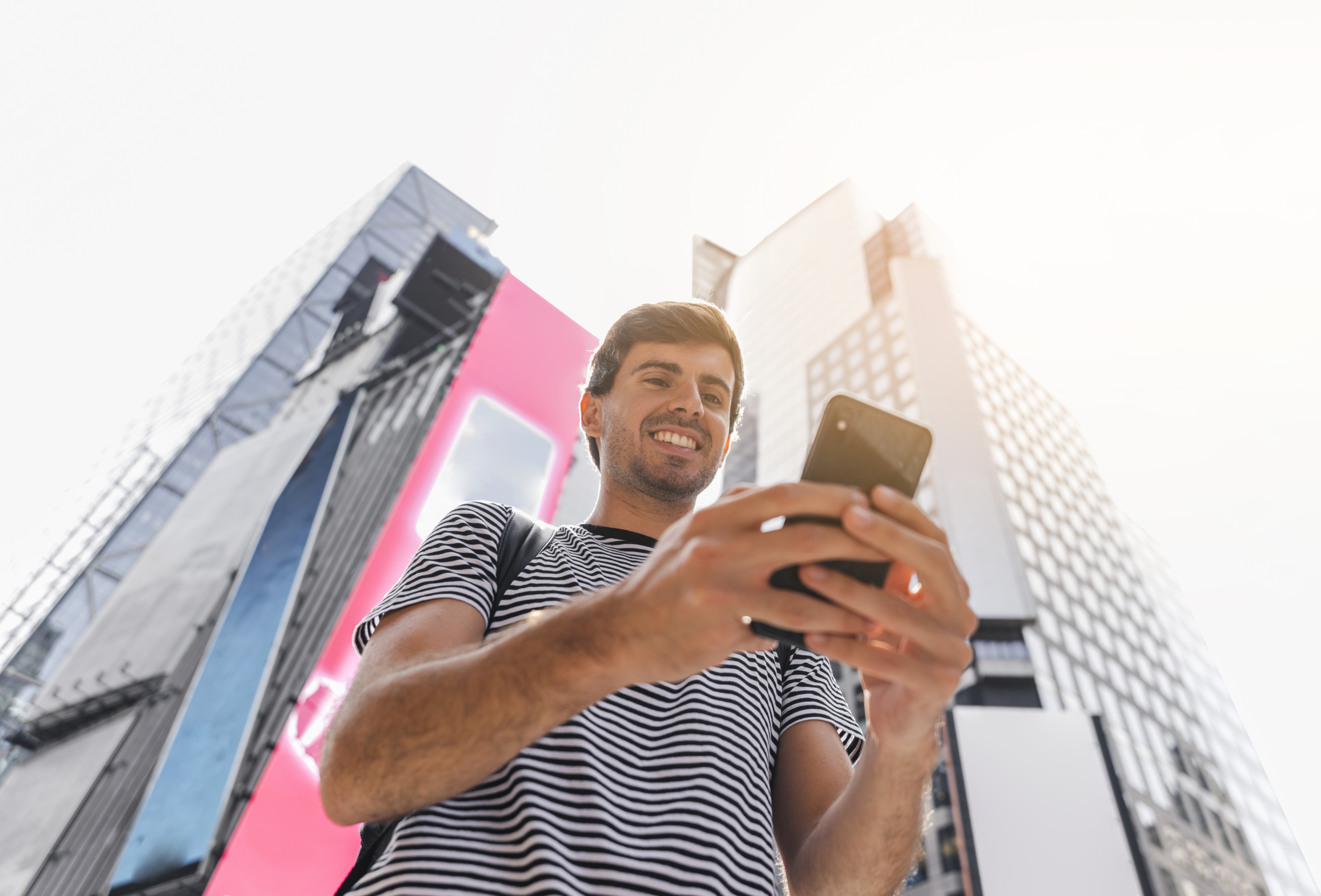 Hombre joven usando el celular con edificios de fondo